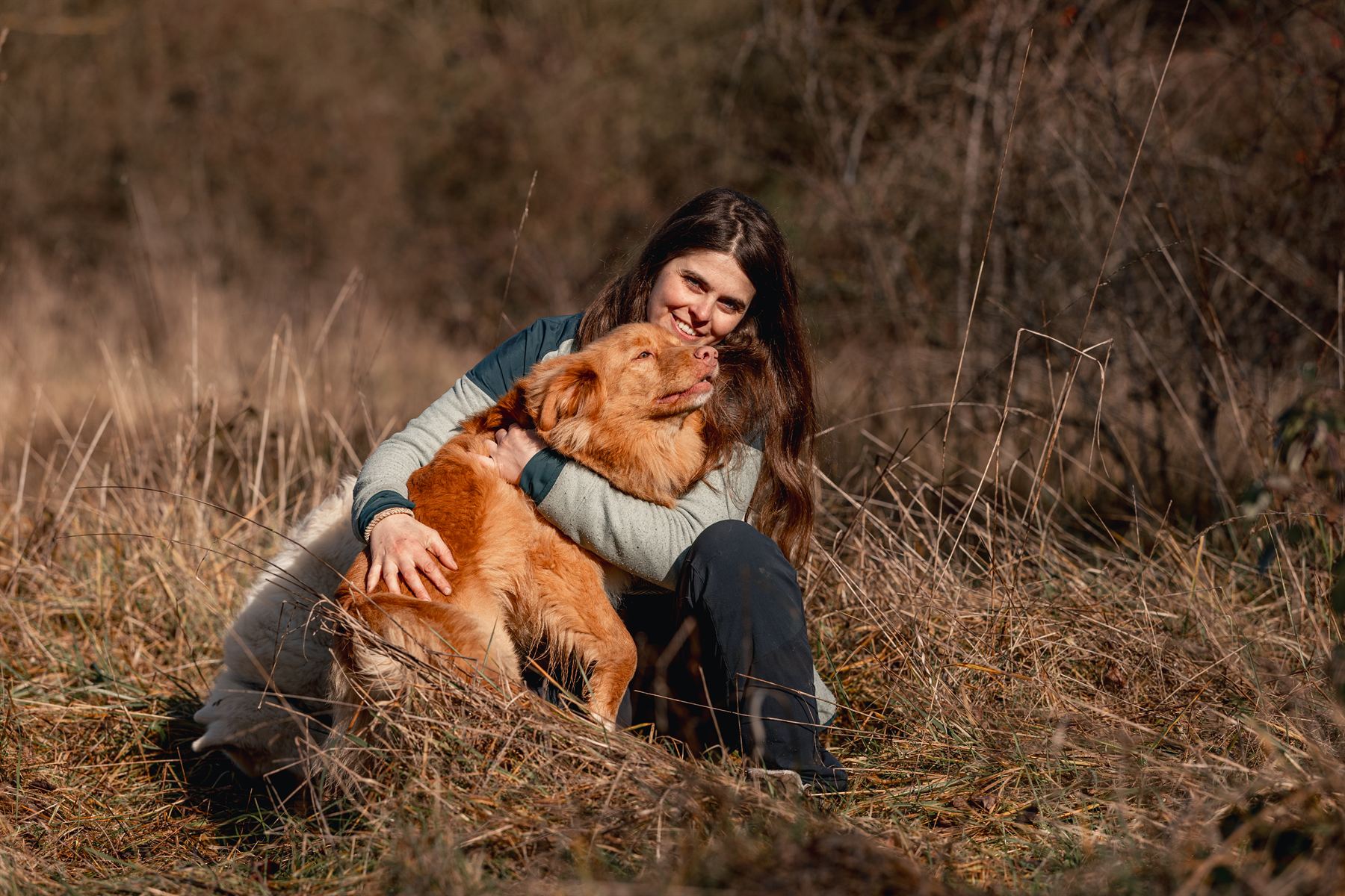 Jeune femme serrant son chien roux dans ses bras, assise dans les herbes sèches