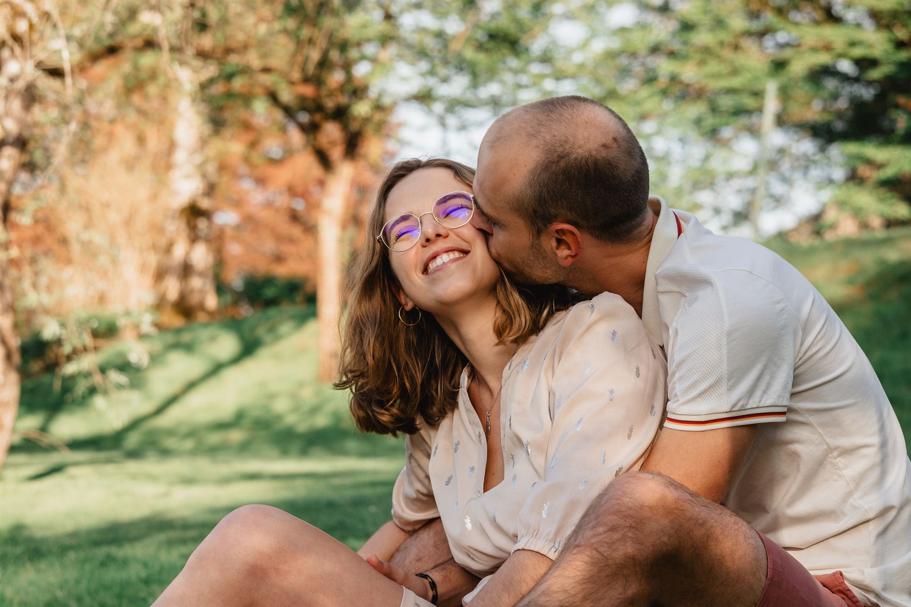 Couple assis dans l'herbe, lui l'embrassant sur la joue