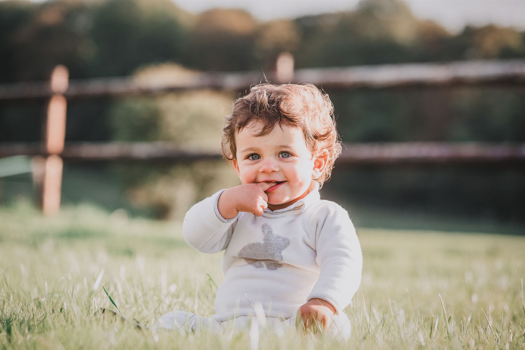 Bébé souriant assis dans l'herbe devant une barrière en bois