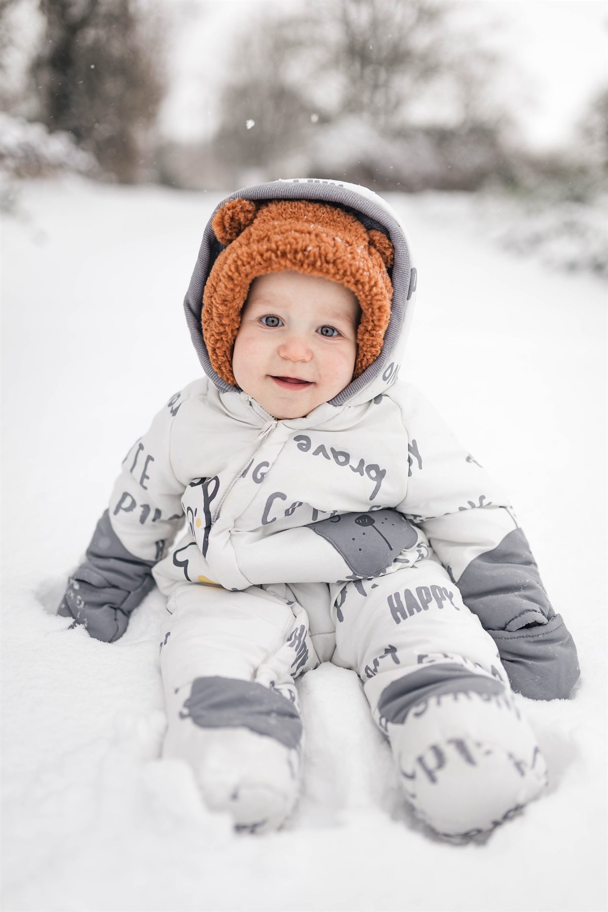Bébé souriant assis dans la neige, combinaison blanche et bonnet ourson