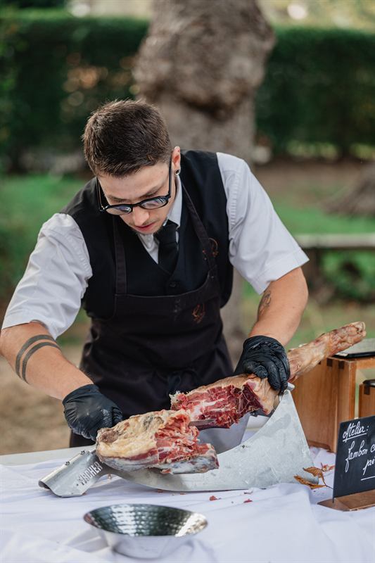 Traiteur découpant un jambon lors d'une réception en plein air