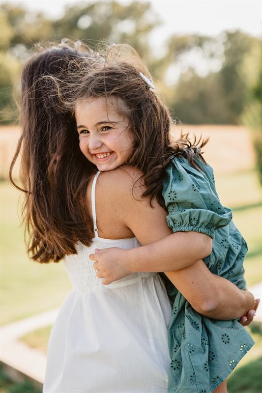 Fillette riant, accrochée au cou de sa maman