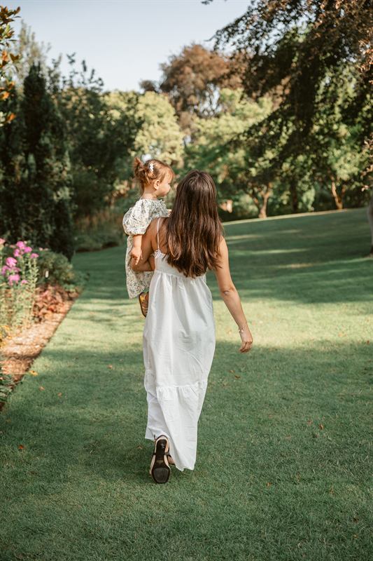 Maman portant sa fille dans une allée de jardin, vue de dos