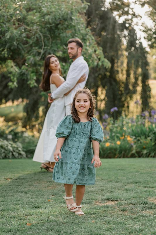 Fillette en robe verte au premier plan, ses parents enlacés derrière