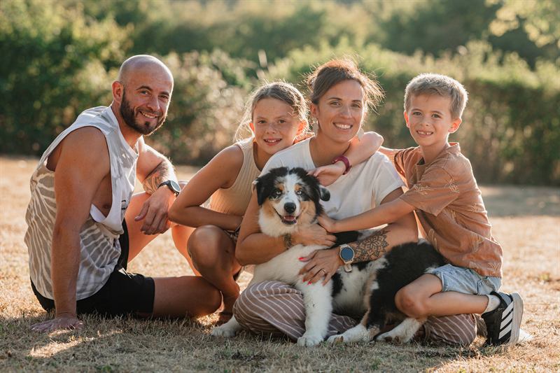 Famille de quatre et leur berger australien assis dans l'herbe au soleil