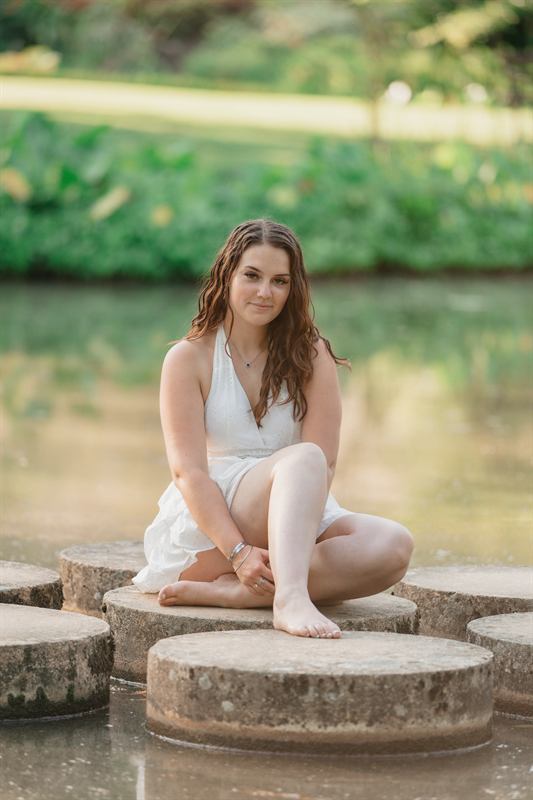 Jeune femme assise en tailleur sur une pierre au milieu de l'eau