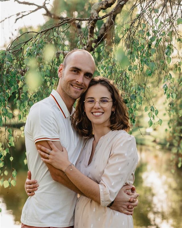 Couple souriant enlacé sous un saule, au bord de l'eau
