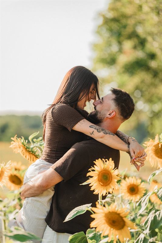 Couple s'embrassant, elle dans ses bras, champ de tournesols